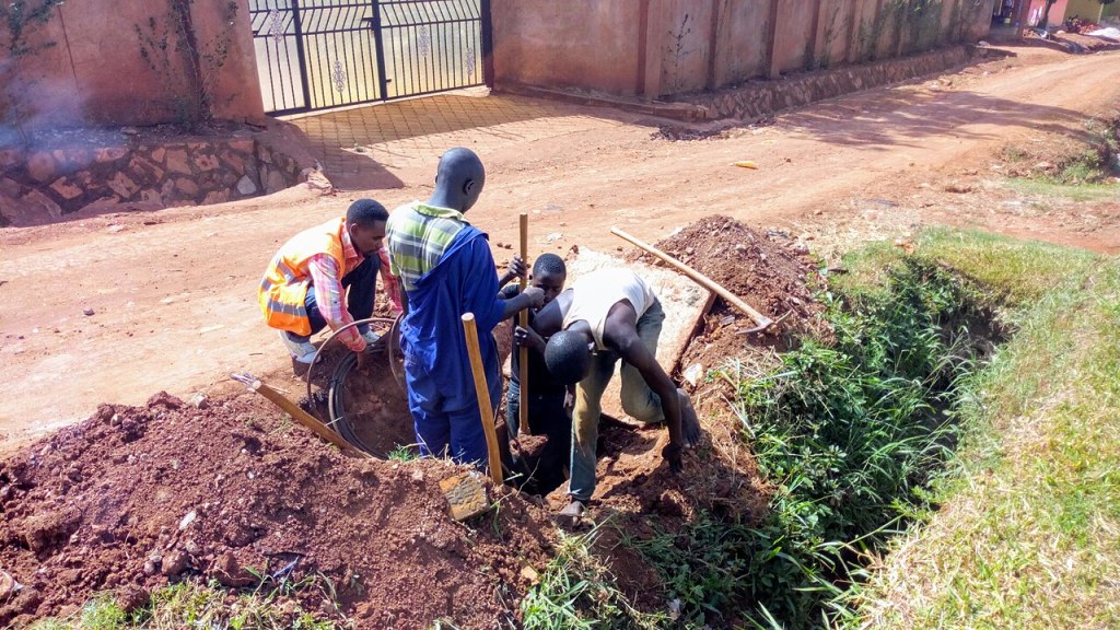 Fiber-optic workers clearing and servicing an underground fiber manhole along a road in Uganda