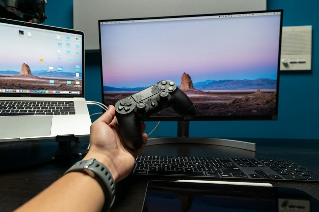Realistic photograph of a person holding a game controller in front of a gaming setup.