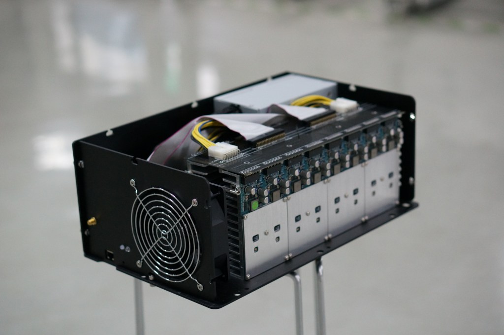 Early Avalon1 ASIC Bitcoin mining machine with exposed modular hashing boards and cooling fan.