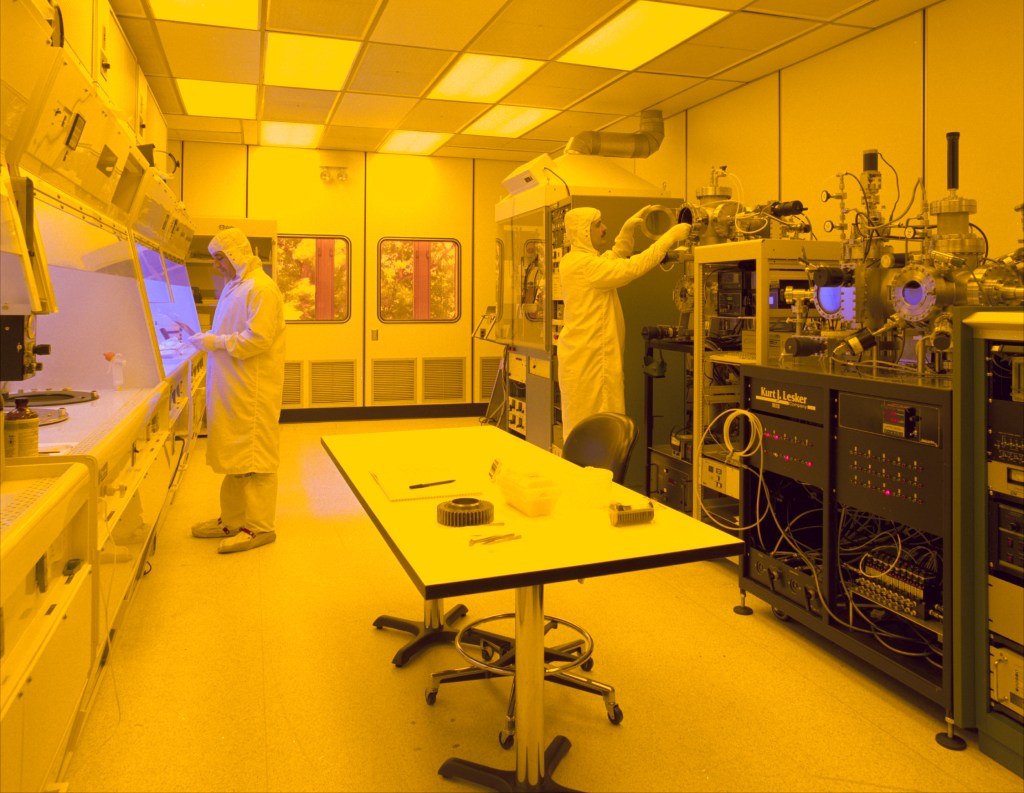 Semiconductor manufacturing cleanroom with technicians operating fabrication equipment.