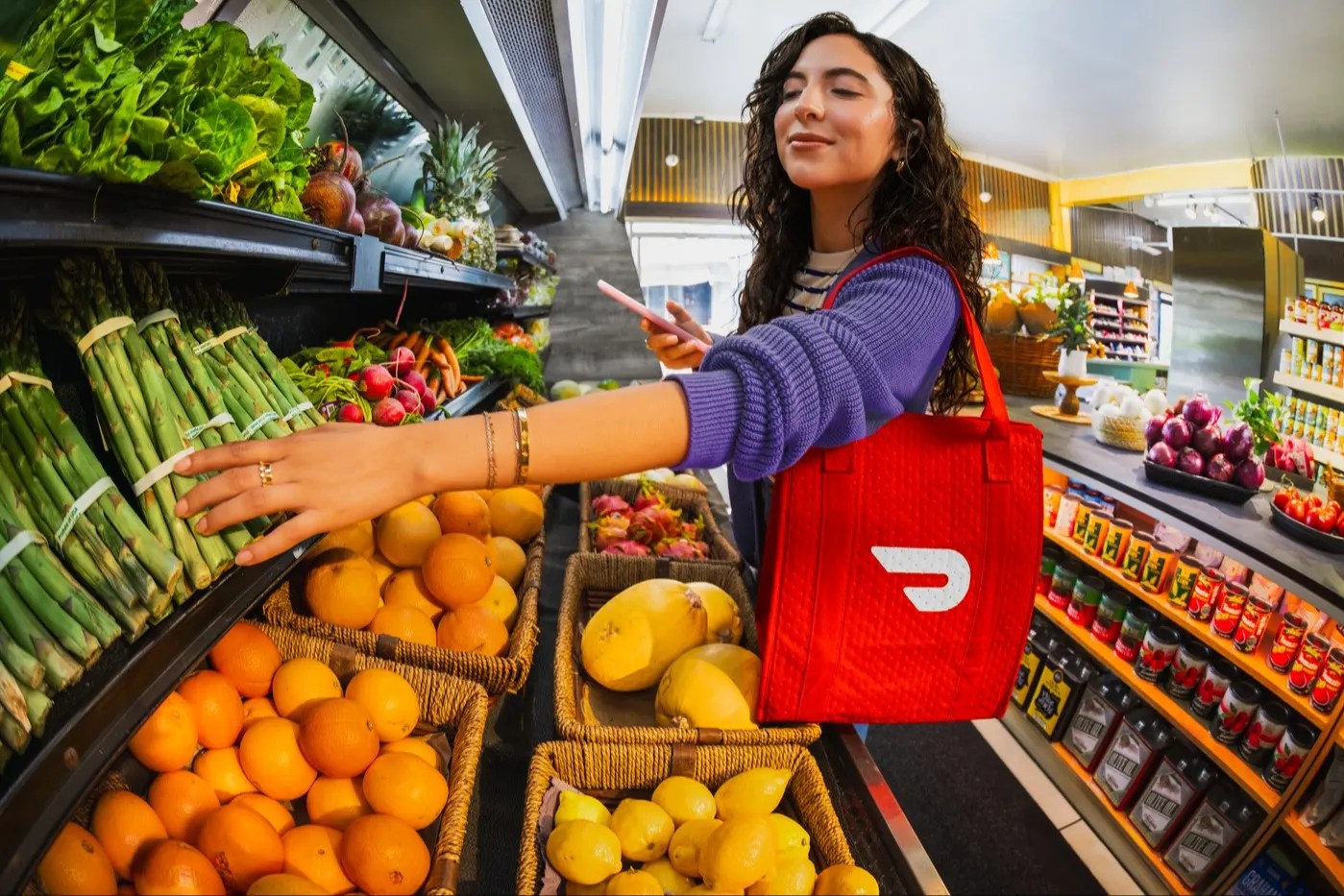 DoorDash shopper with red insulated bag choosing produce in a grocery store