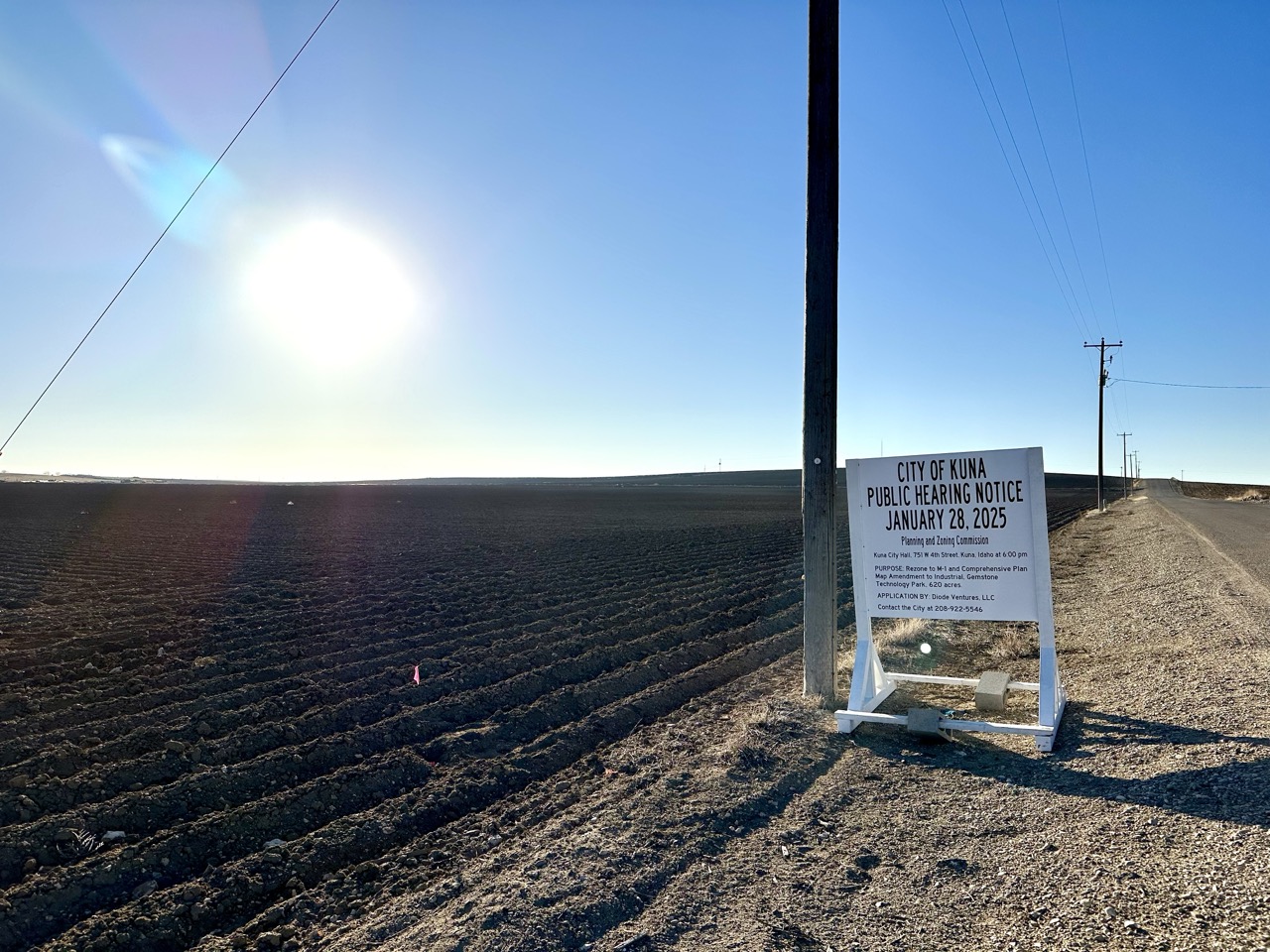Kuna public hearing sign by an agricultural field and gravel roadside