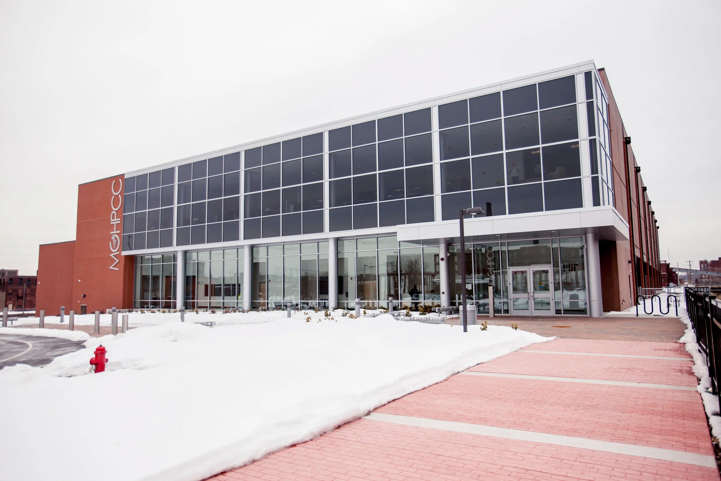 Actual MGHPCC research computing building exterior in Holyoke with glass facade, brick MGHPCC signage, and snow-covered plaza
