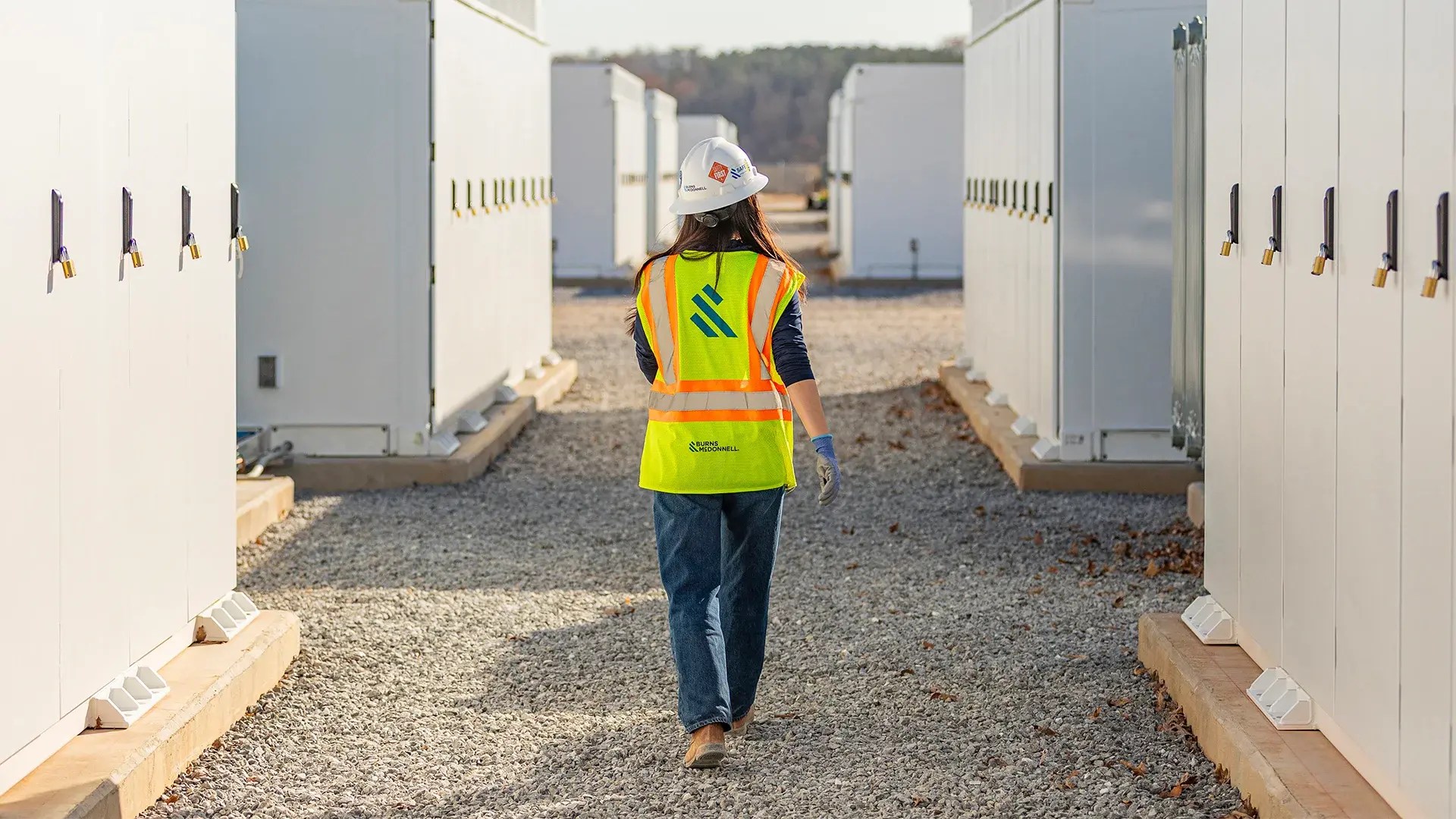 Burns and McDonnell engineer walking between white battery units at McGrau Ford battery storage construction site