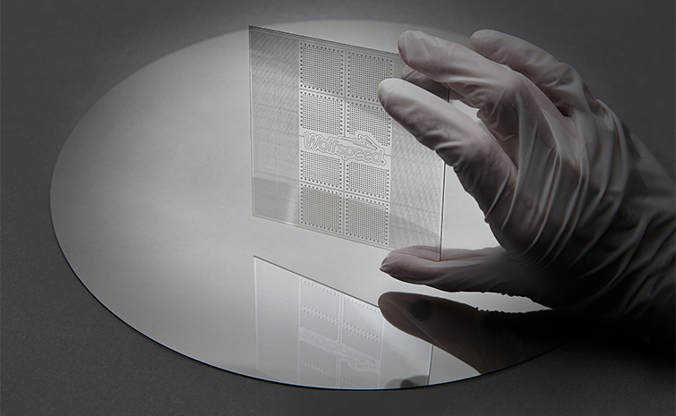 Wolfspeed gloved technician holding a transparent silicon carbide sample above a larger reflective wafer