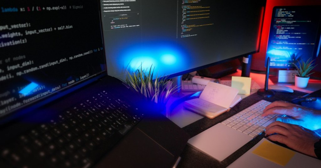 Programmer working at a dark multi-monitor coding workstation.