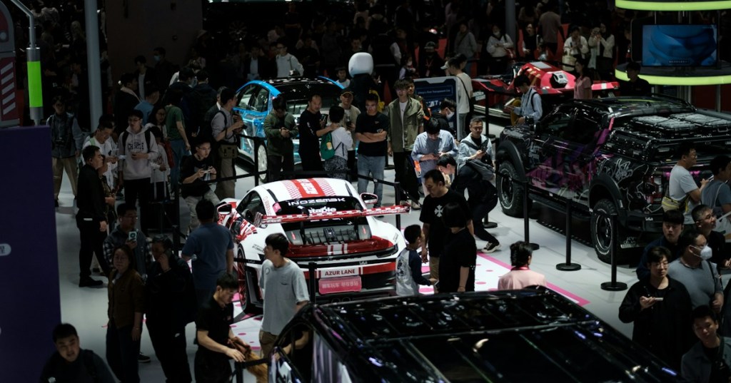 Crowds examining new cars at a large indoor auto show