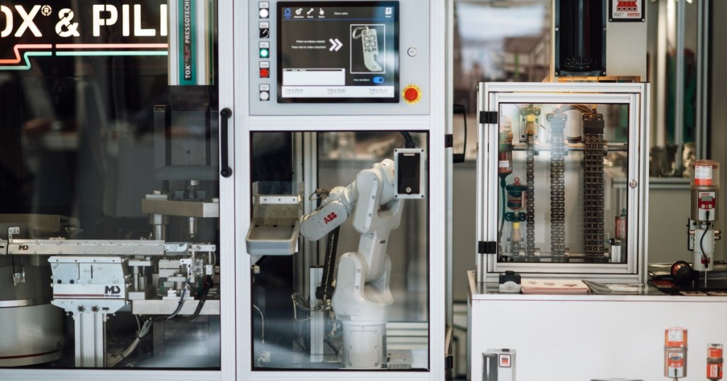 Industrial robotic arm operating machinery in a factory, used as the featured image for a robotics feedback-control lesson.