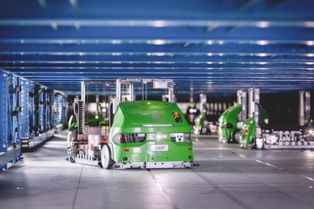 Green Symbotic autonomous mobile warehouse robots operating within automated blue storage racks