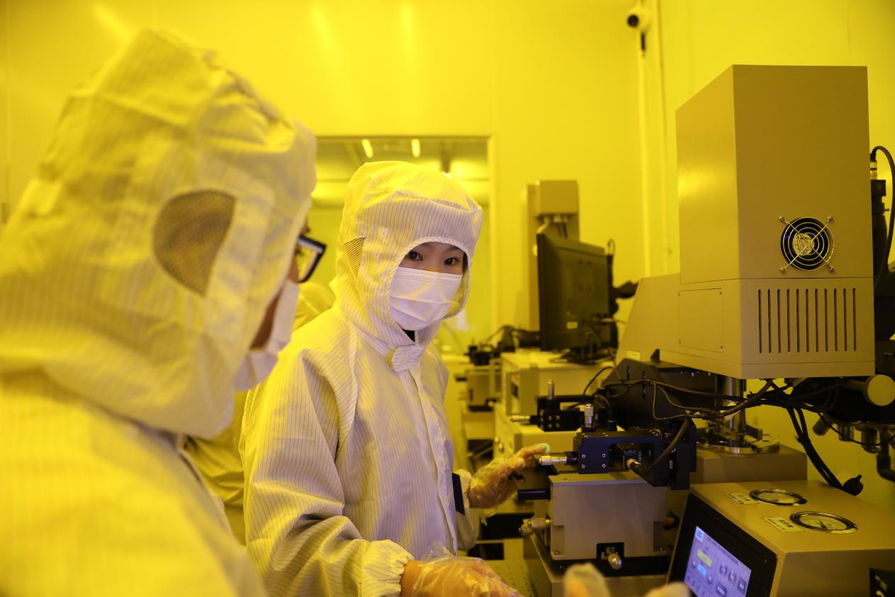 Researchers in a yellow-lit cleanroom at Tsinghua University's Micro-Nano Fabrication Center operating semiconductor processing equipment