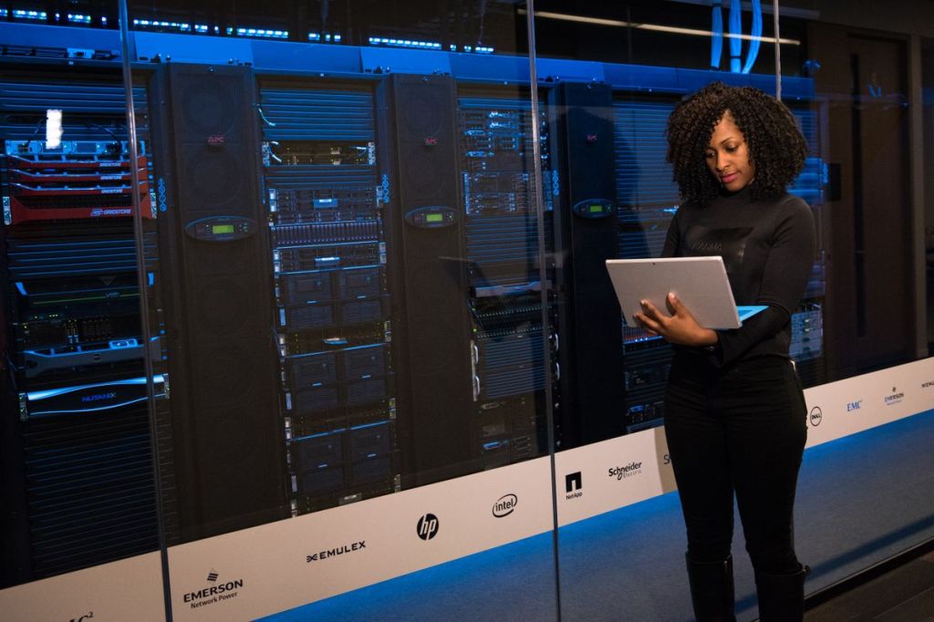 Engineer using a laptop while monitoring server racks in a data center.