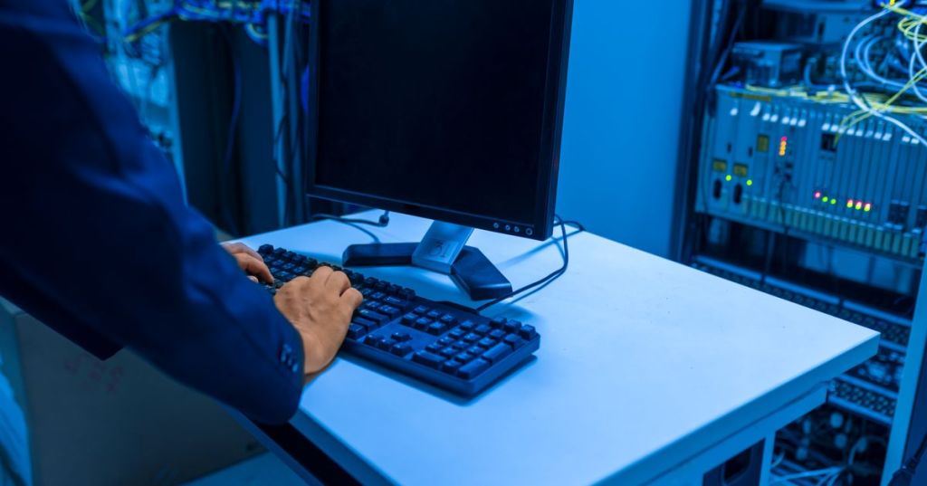 IT professional operating a workstation beside server hardware in a data center.