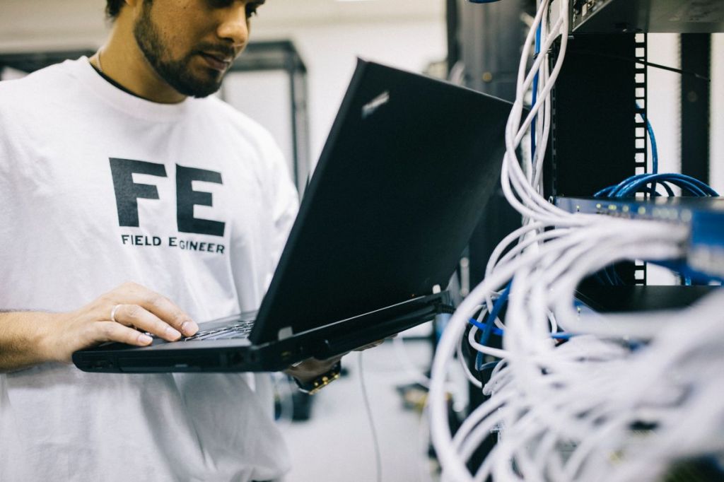Field engineer using a laptop while working beside server and network hardware.