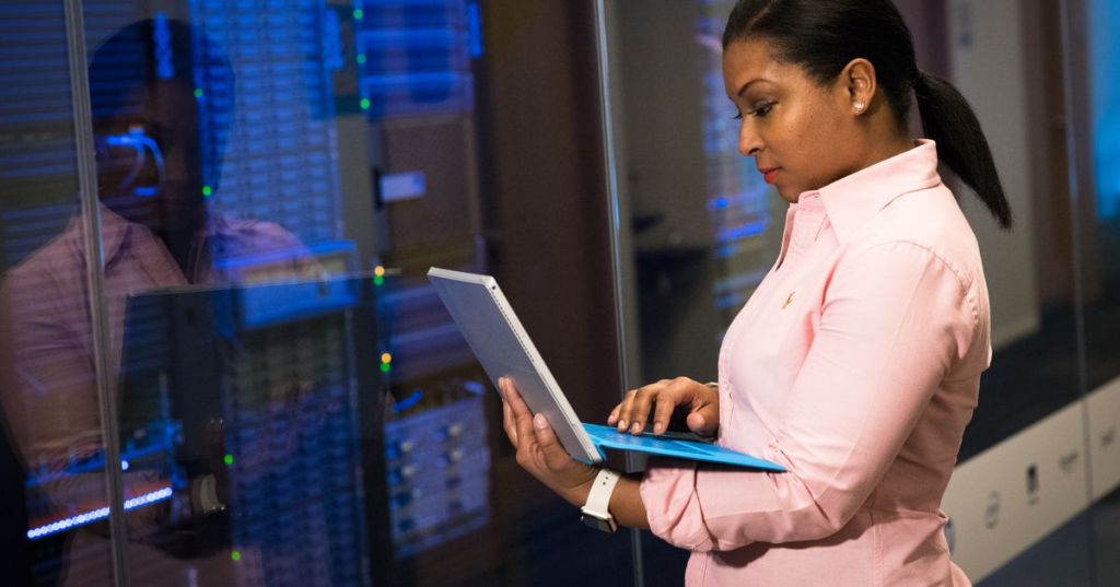 System administrator working on a laptop inside a server room.
