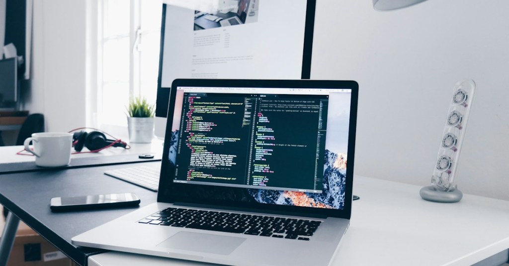 Editorial photograph of a laptop displaying source code in a technical workspace.