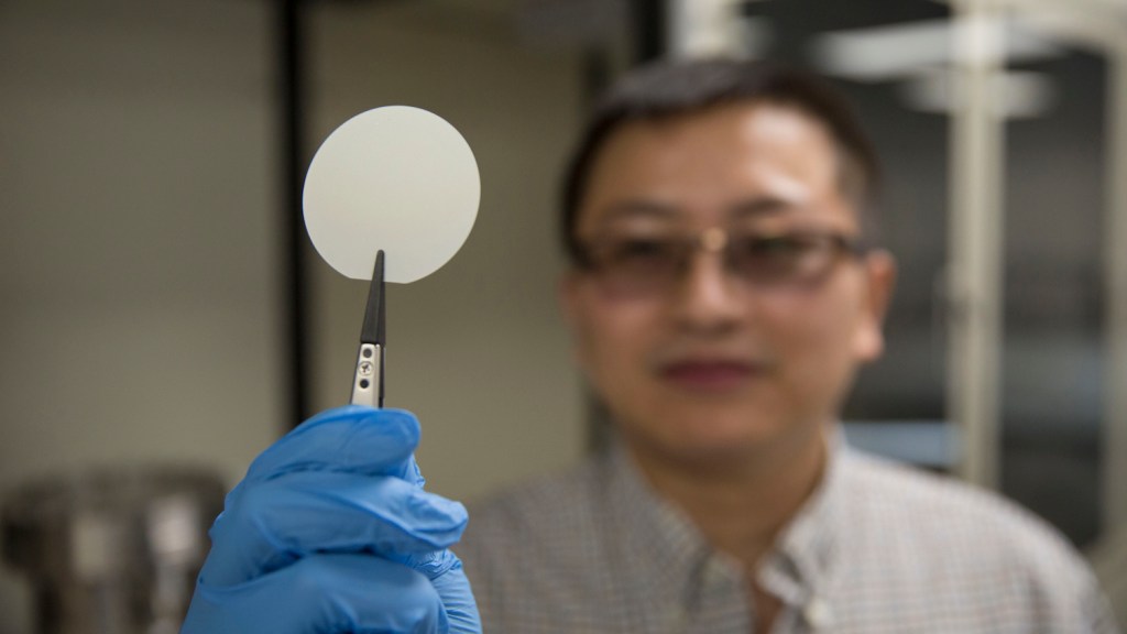 Yuji Zhao holding a gallium nitride wafer in an Arizona State University semiconductor laboratory